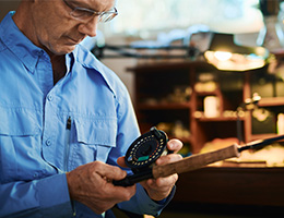 A man in a workshop holds a fishing rod. 