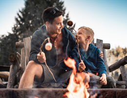 A man and a boy toast marshmallows over a fire.