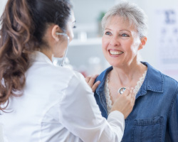 A doctor holds a stethoscope to a woman’s chest.