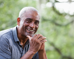 A man rests his chin on his thumbs, smiling.