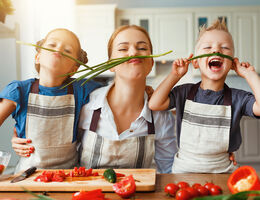 A woman and two kids wearing aprons show off chive mustaches.