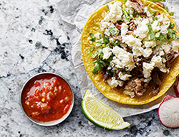 Tostadas topped with meat, lettuce and queso fresco surrounded by limes, radishes and salsa.