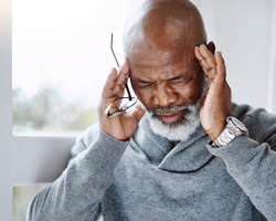 An older adult putting his fingers to his head and grimacing.