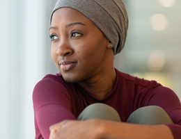 A woman in a head scarf hugs her knees to her chest.