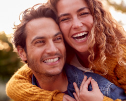 A smiling woman hugs a smiling man from behind