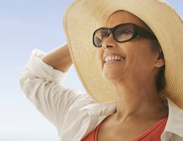 A woman standing outside wearing a hat, sunglasses and a long-sleeved shirt.