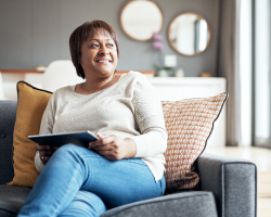 A woman sits on a couch, holding a tablet.