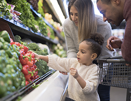 A young family shopping in the veggie section of a grocery store. 